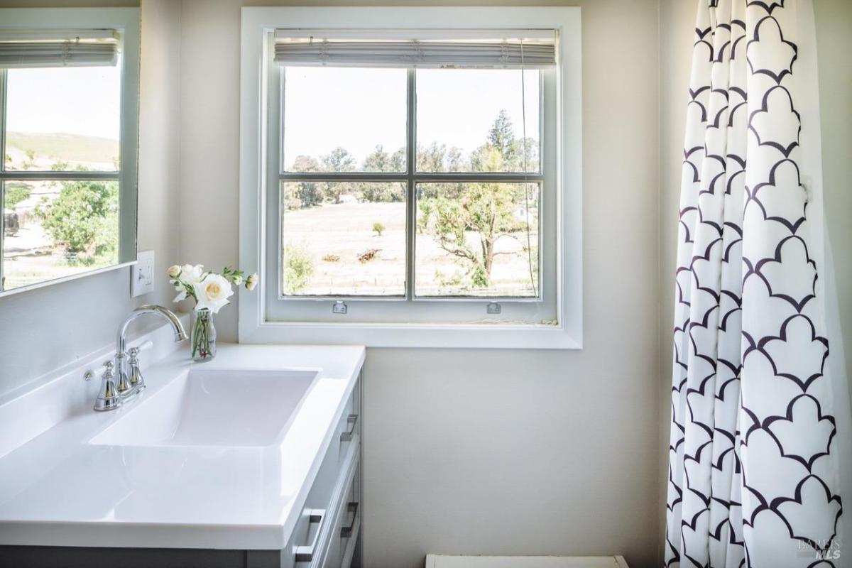 A bathroom with a white sink, window view, and patterned shower curtain.