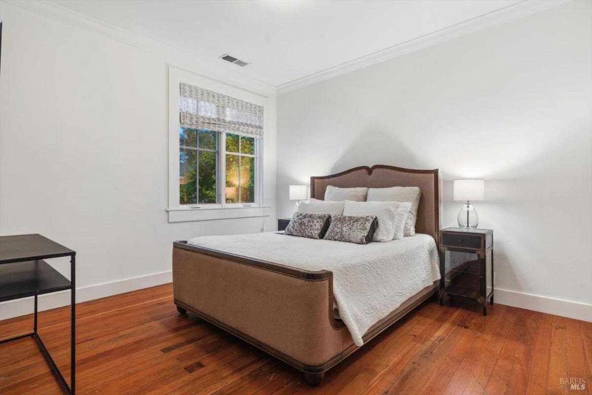 A bedroom bed with a wooden frame and two windows with blinds.