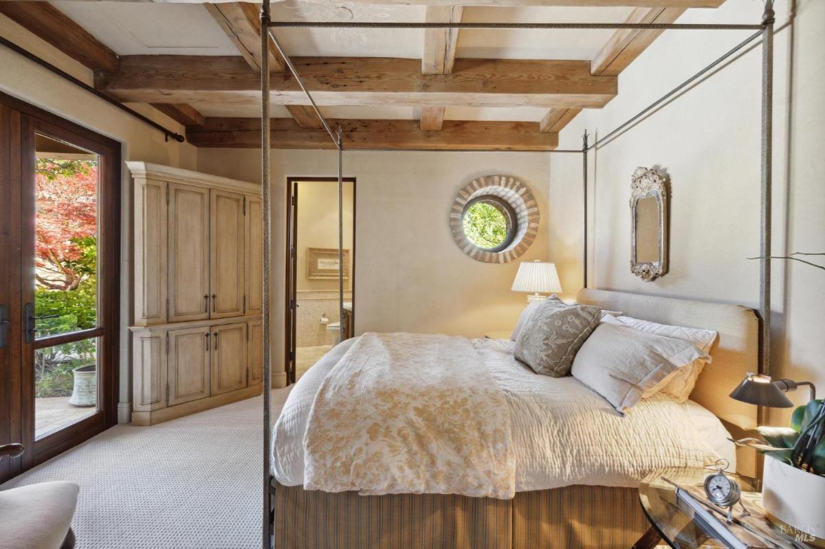  A bedroom with a four-poster bed, wooden dresser, large window, and exposed wooden beams.