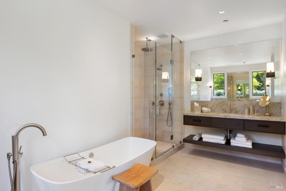 A bathroom with freestanding bathtub with a floor-mounted faucet and a glass-enclosed shower beside a double-sink vanity.