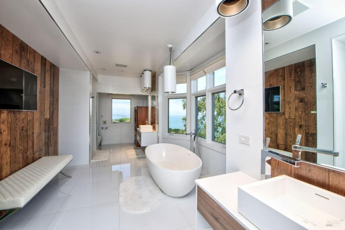 A bathroom with a freestanding bathtub, double sinks, and large windows.