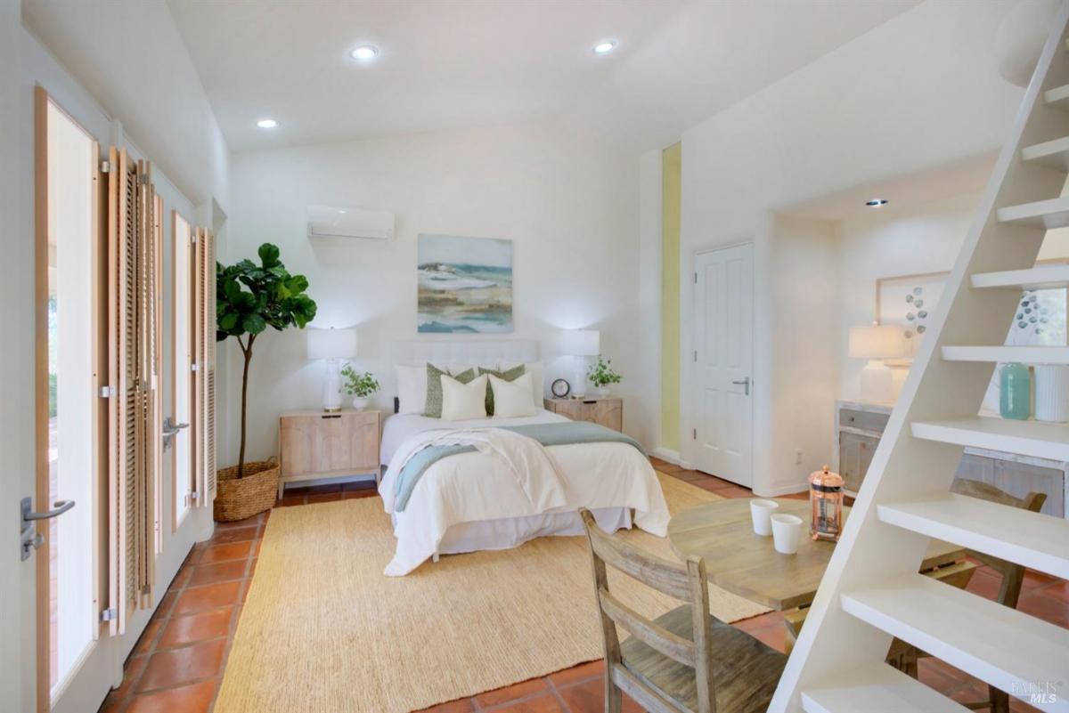 A bedroom with a ladder leading to a loft, doors opening to a patio.