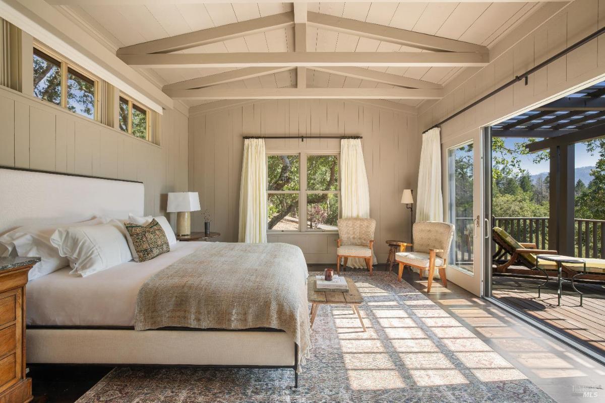 Bedroom with a vaulted ceiling, large windows, and access to a balcony.