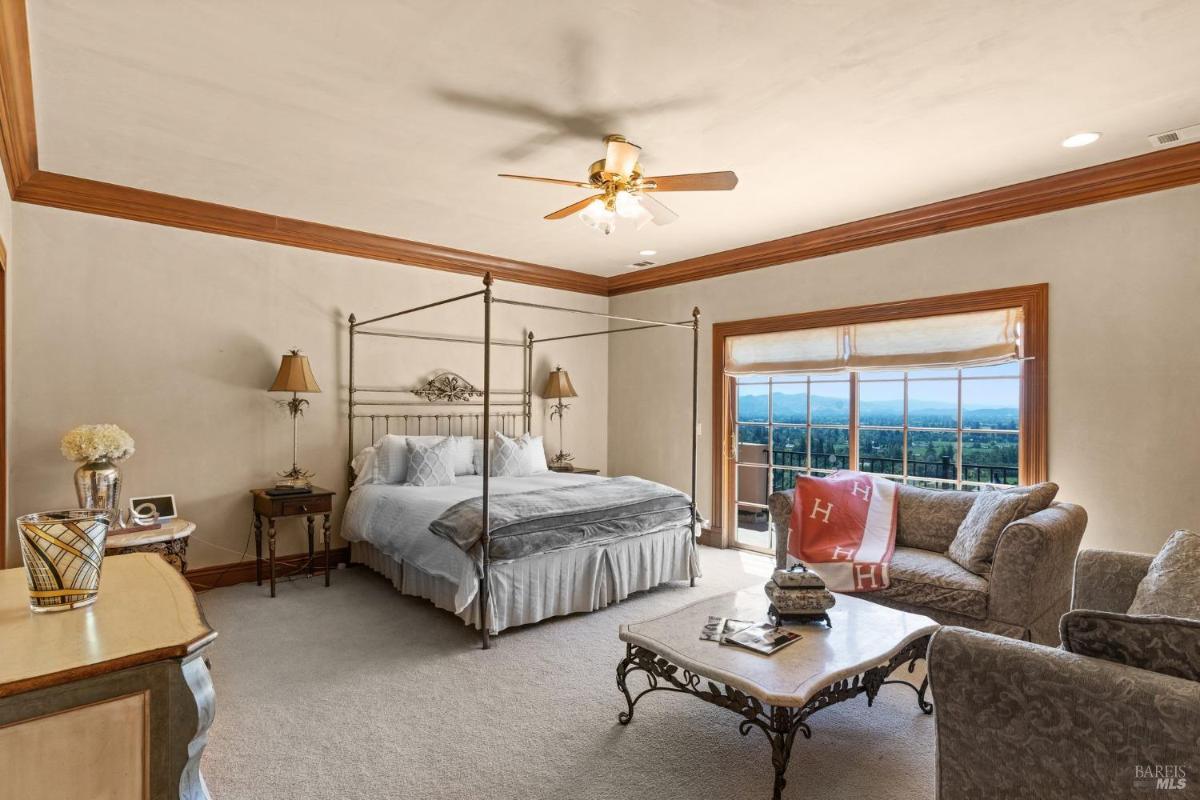 Bedroom with a metal-framed bed, sofa seating, and balcony access overlooking the landscape.