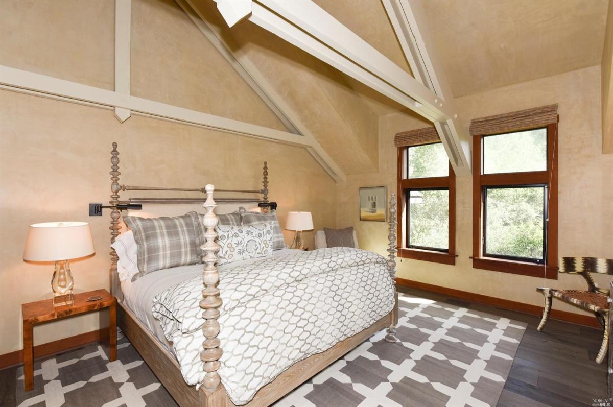 A bedroom with a bed featuring decorative posts, two windows, and a geometric patterned rug.