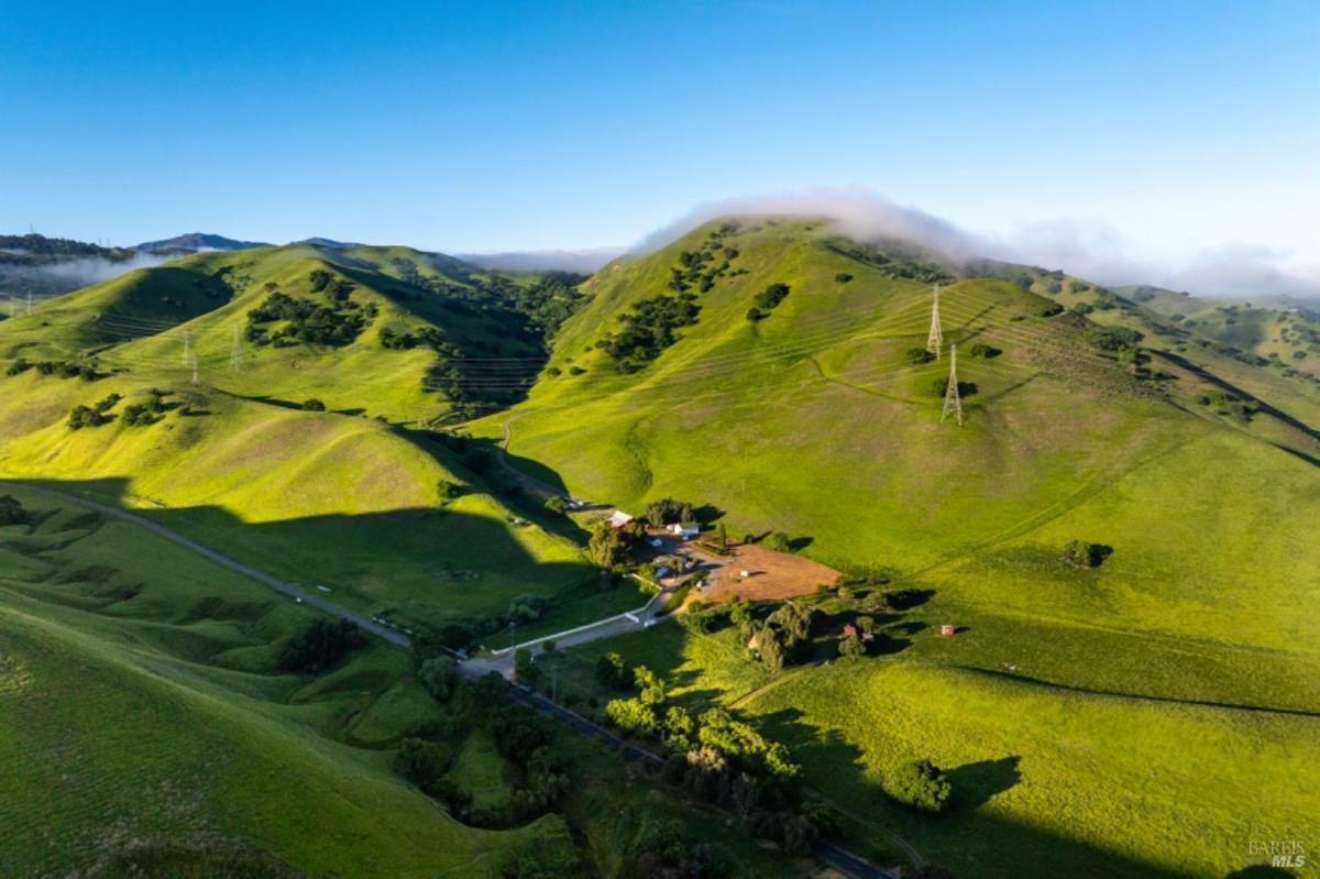 Expansive view of rolling green hills with a small ranch in the valley.