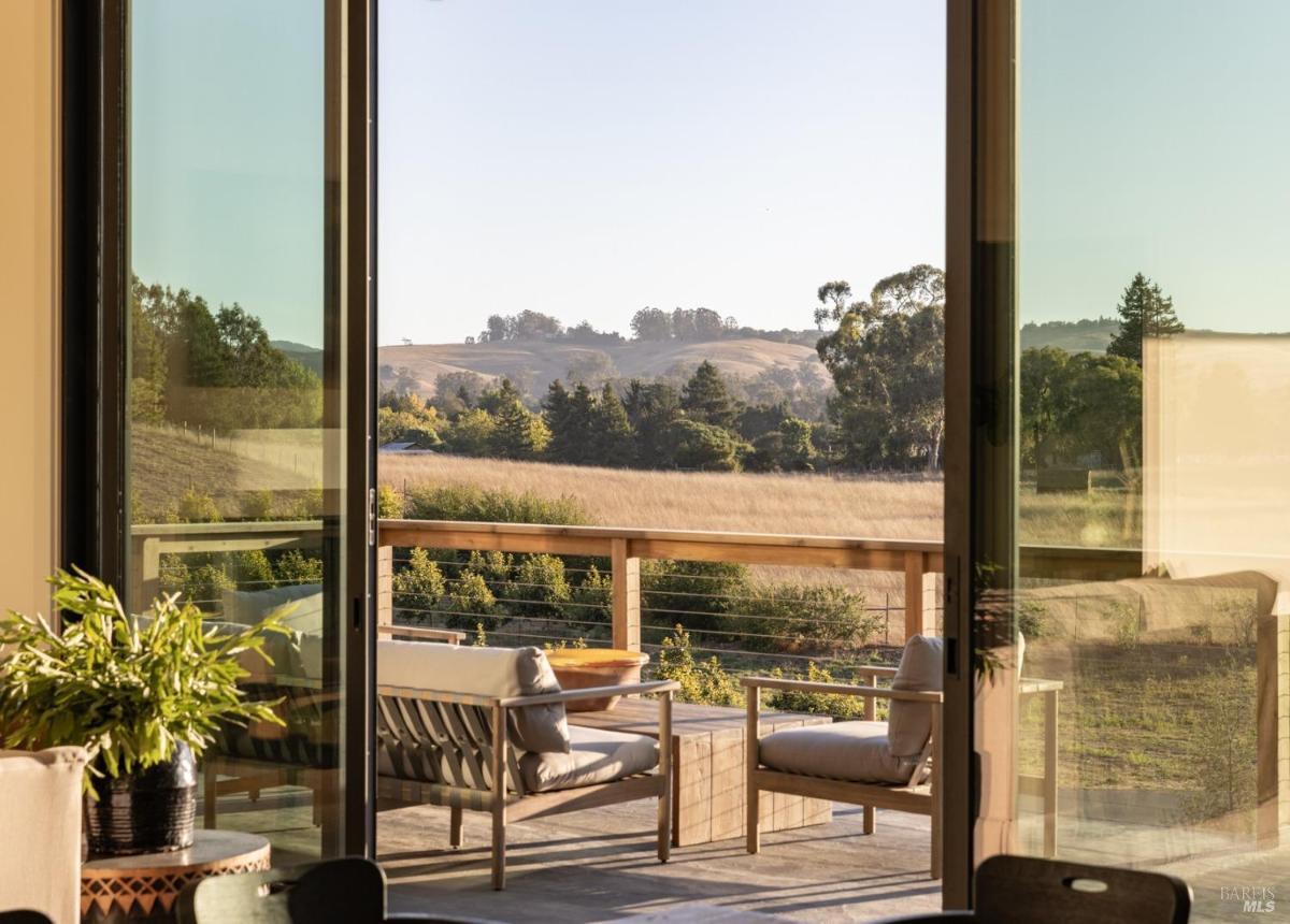 A view through large windows shows a deck with seating and a grassy landscape outside.