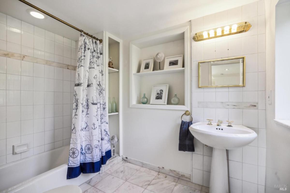 Bathroom with a tub, pedestal sink, and built-in shelves with decor items.