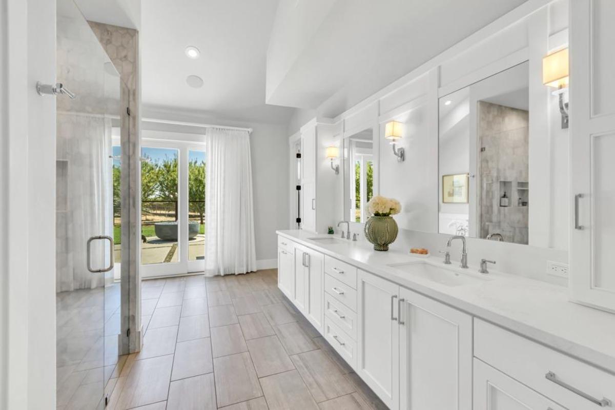 A bathroom with a double vanity, mirrors, and a glass shower enclosure.