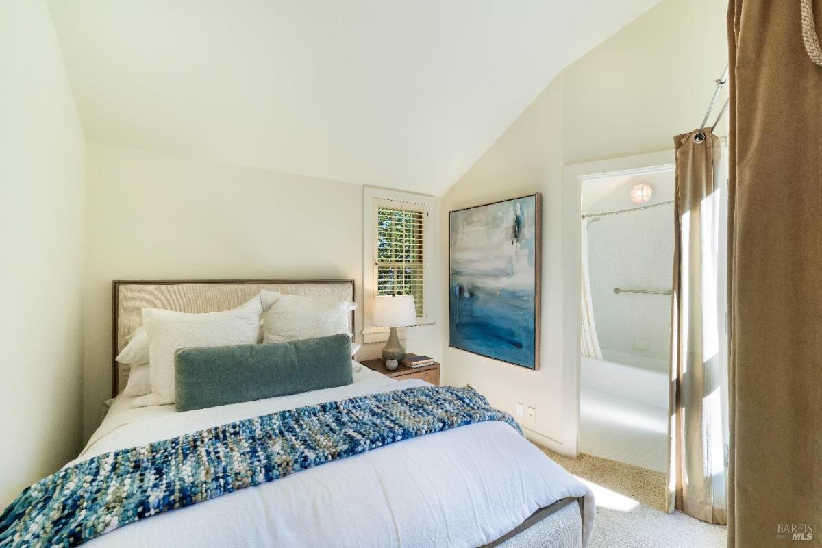 Bedroom with a bed, corner windows, and white shutters.