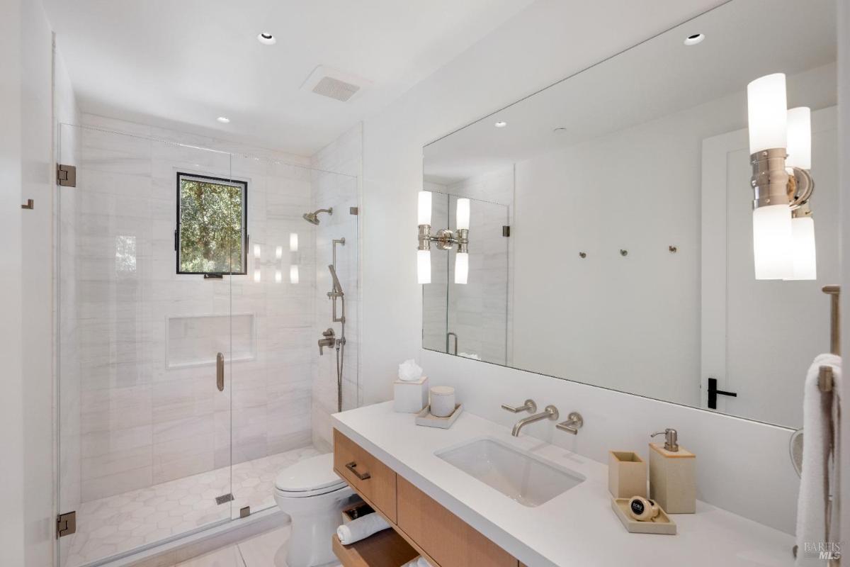 Bathroom with a glass-enclosed shower, a single sink vanity, and a toilet beneath a small window.