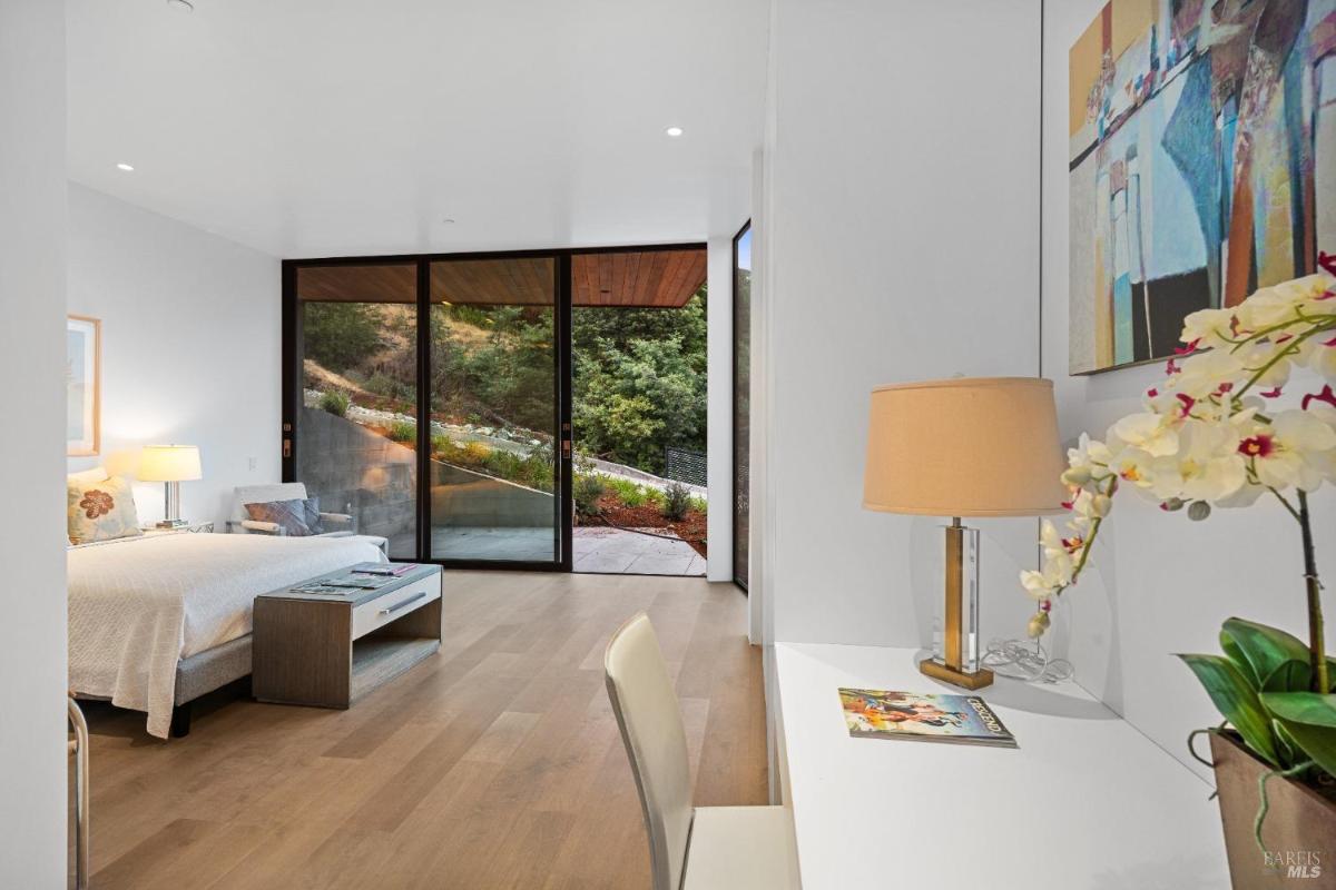 A bedroom with a bench at the foot, and a sliding glass door opening to a hillside view.