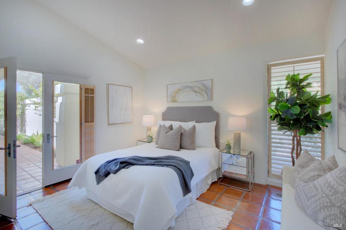 A bedroom with a bed and two glass side tables, doors leading to a private courtyard.