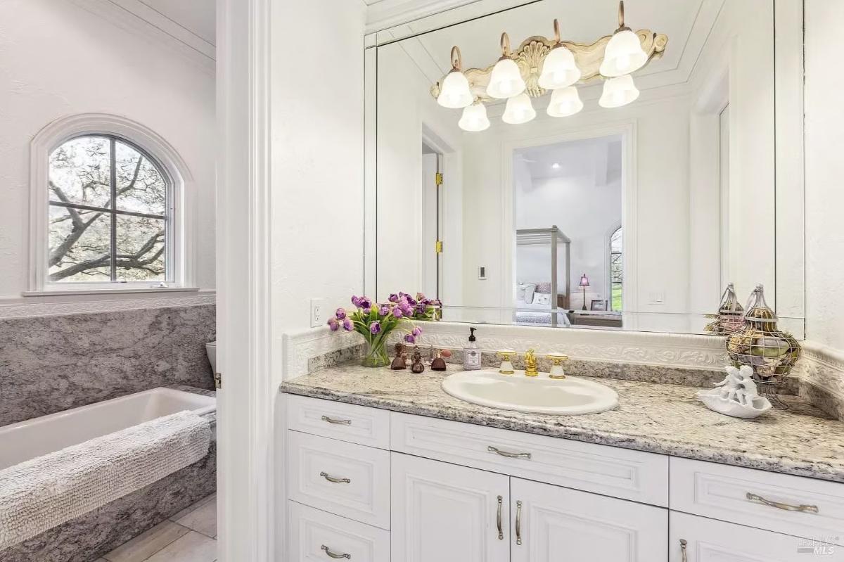 Bathroom featuring a single vanity with granite countertops, a mirrored wall, and a built-in bathtub with a window.