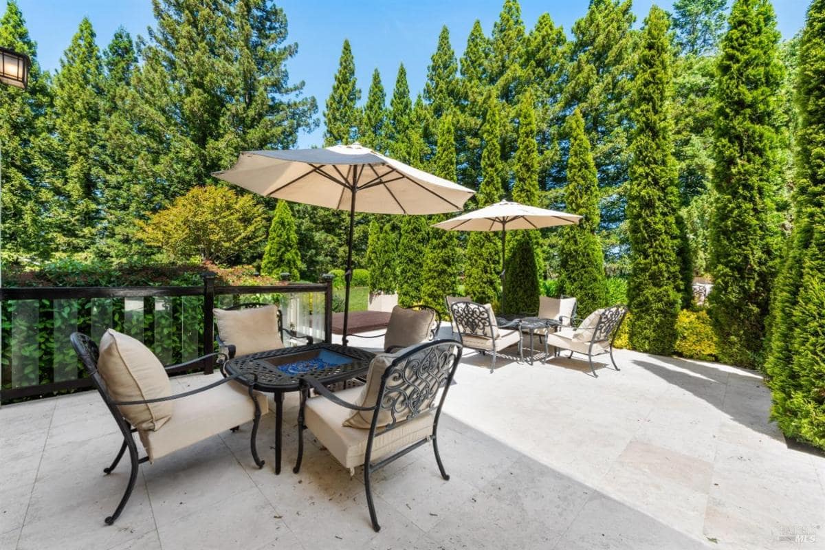 An outdoor terrace with seating areas, umbrellas, and lush greenery in the background. 