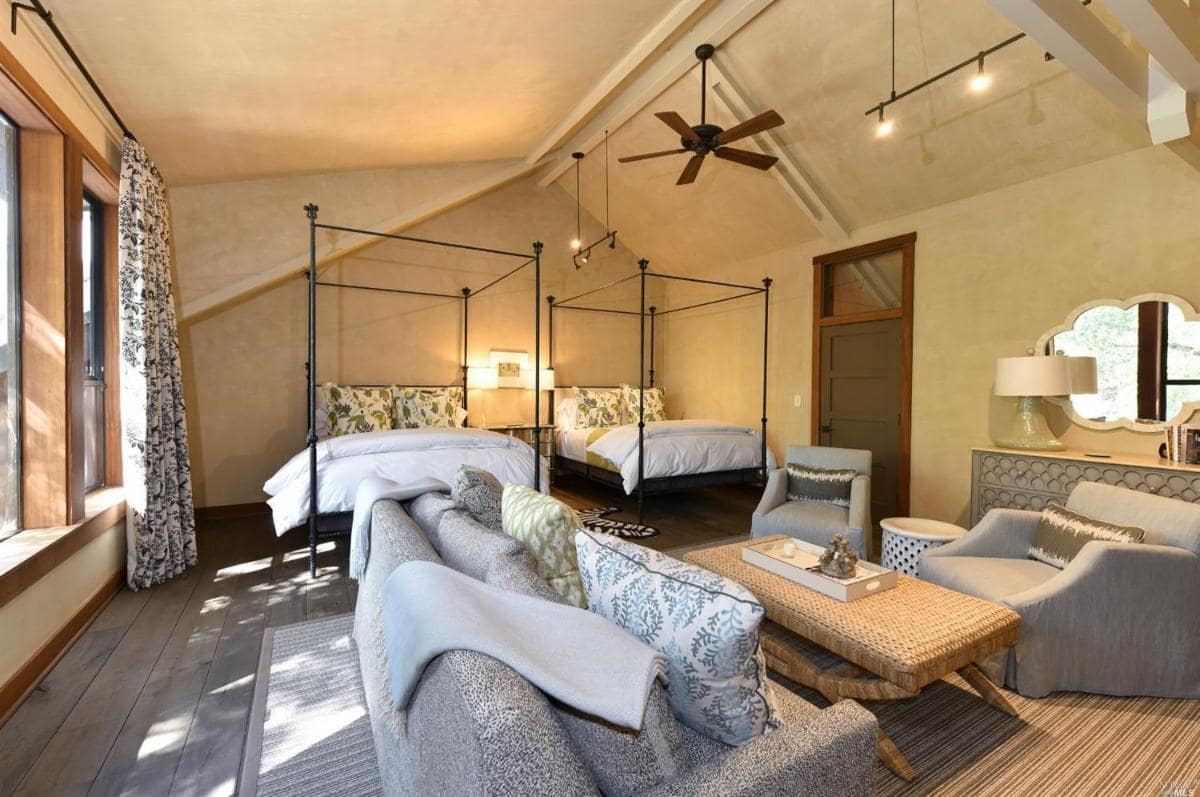 A spacious room with two canopy beds, a seating area, and a ceiling fan.