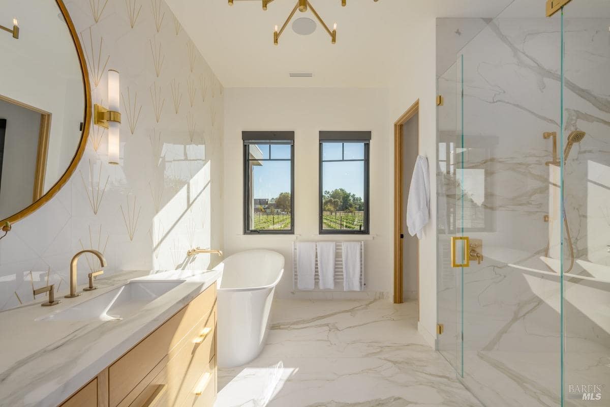 A bathroom with a freestanding tub, double vanity, walk-in shower, and windows facing the vineyard.