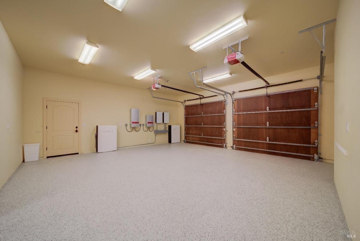 An empty garage with a smooth floor, featuring two large wooden garage doors, wall-mounted utilities, and a door leading outside. 