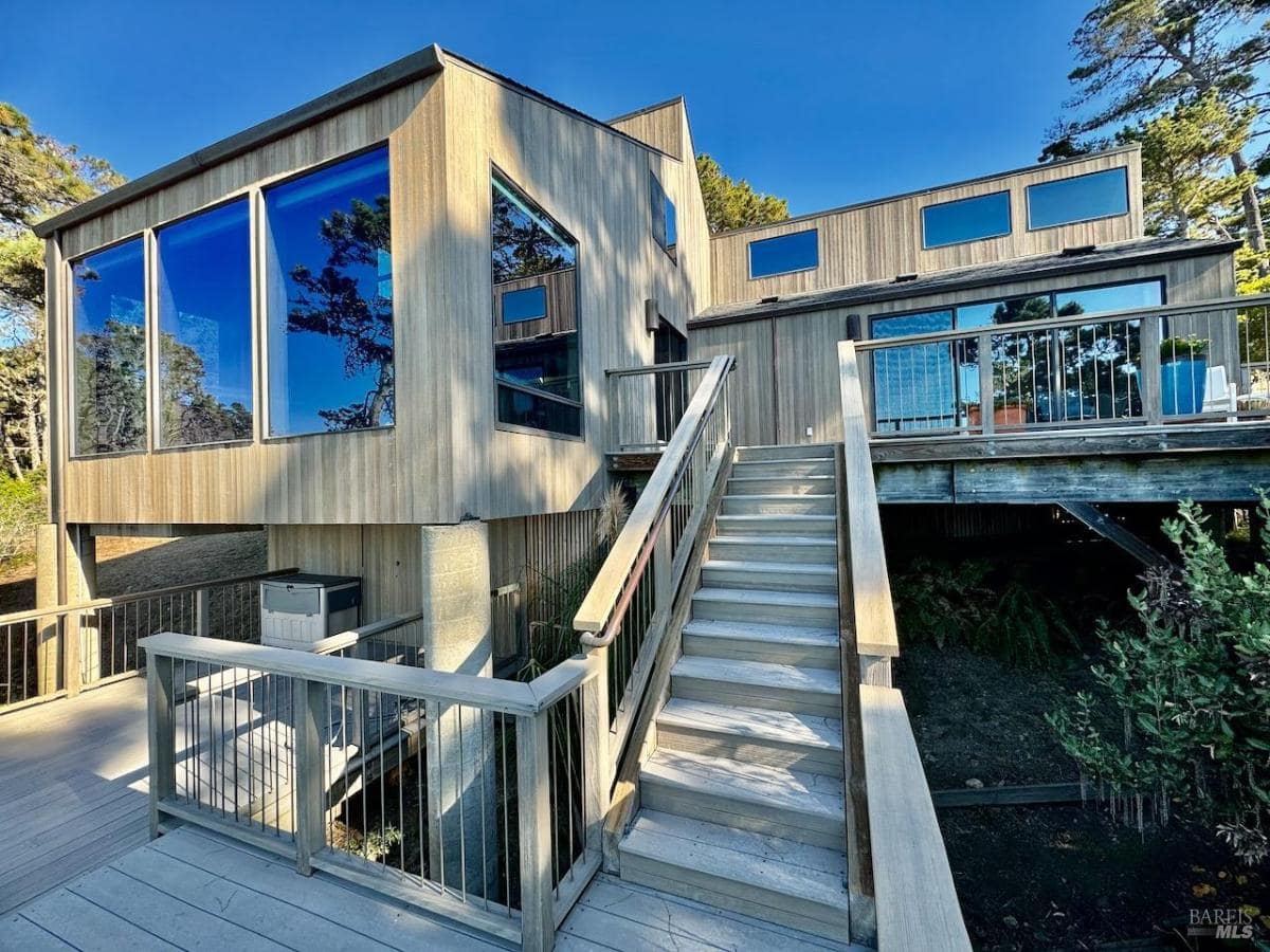 A wooden home exterior with large windows and a staircase leading to the deck.