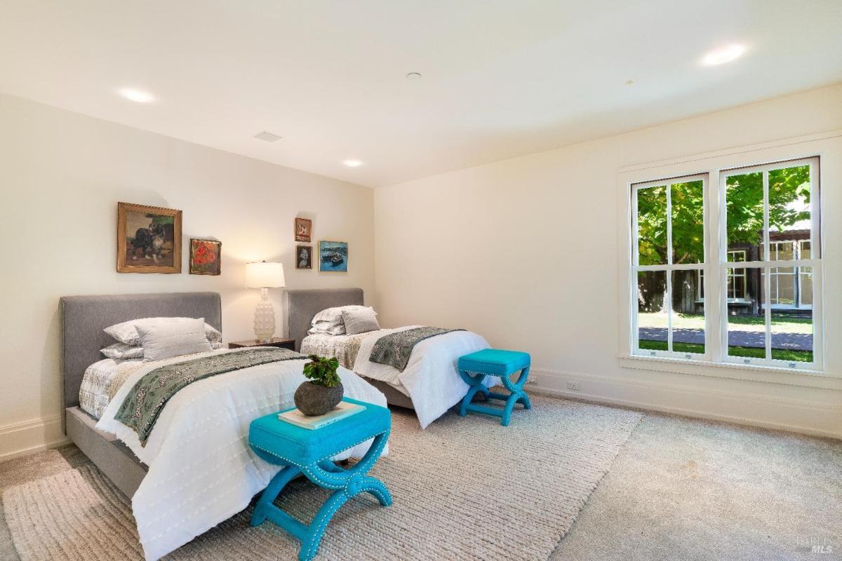 Bedroom with a bed, corner windows, and white shutters.