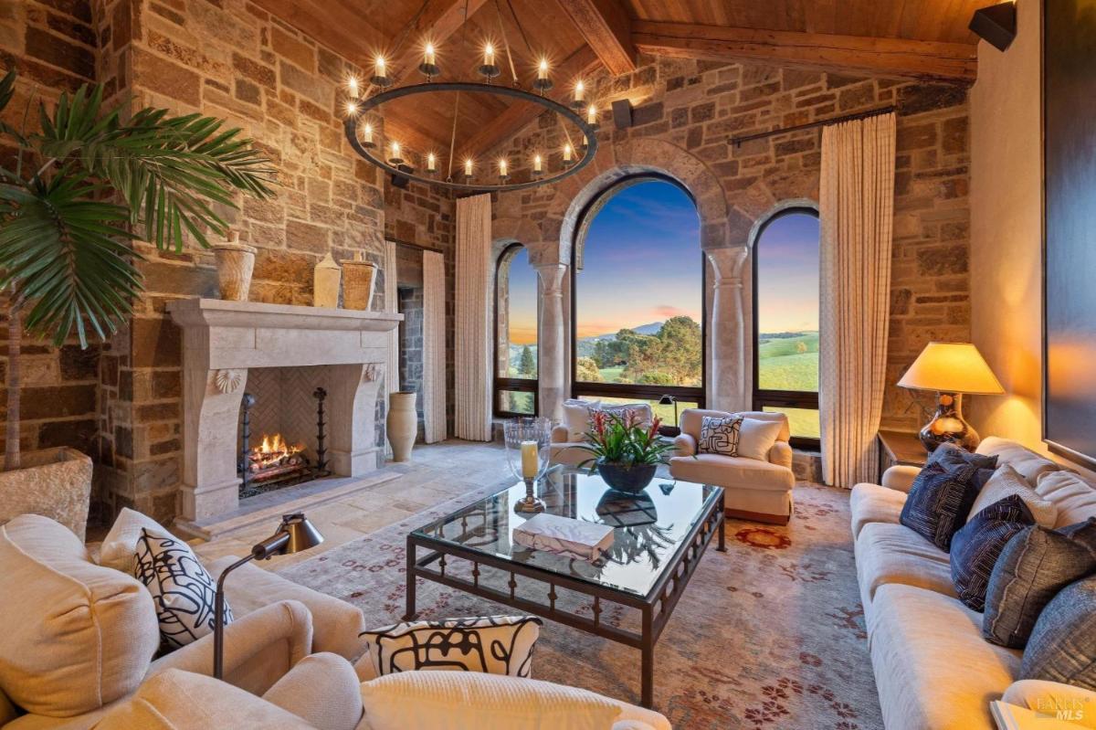 A living room with a stone fireplace, arched windows, and countryside views.