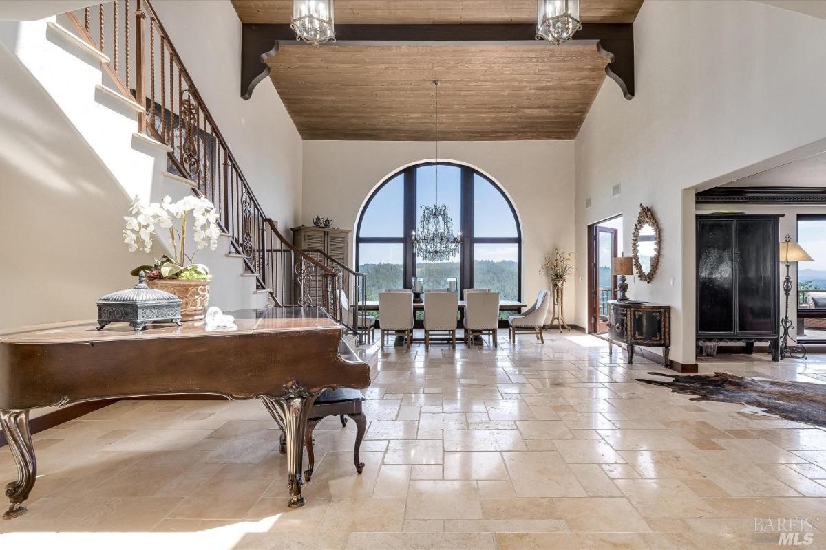 Foyer with staircase, grand piano, and large arched window.