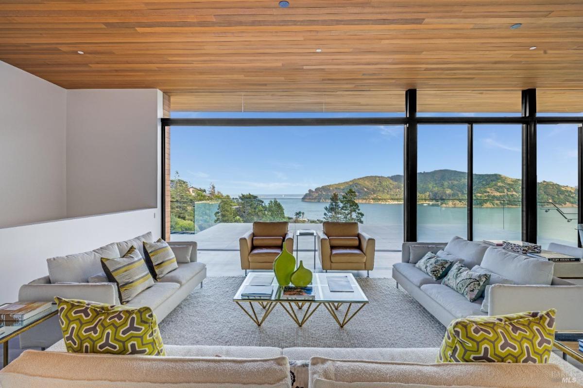 A living room facing large glass windows, with overlooking view and distant hills.