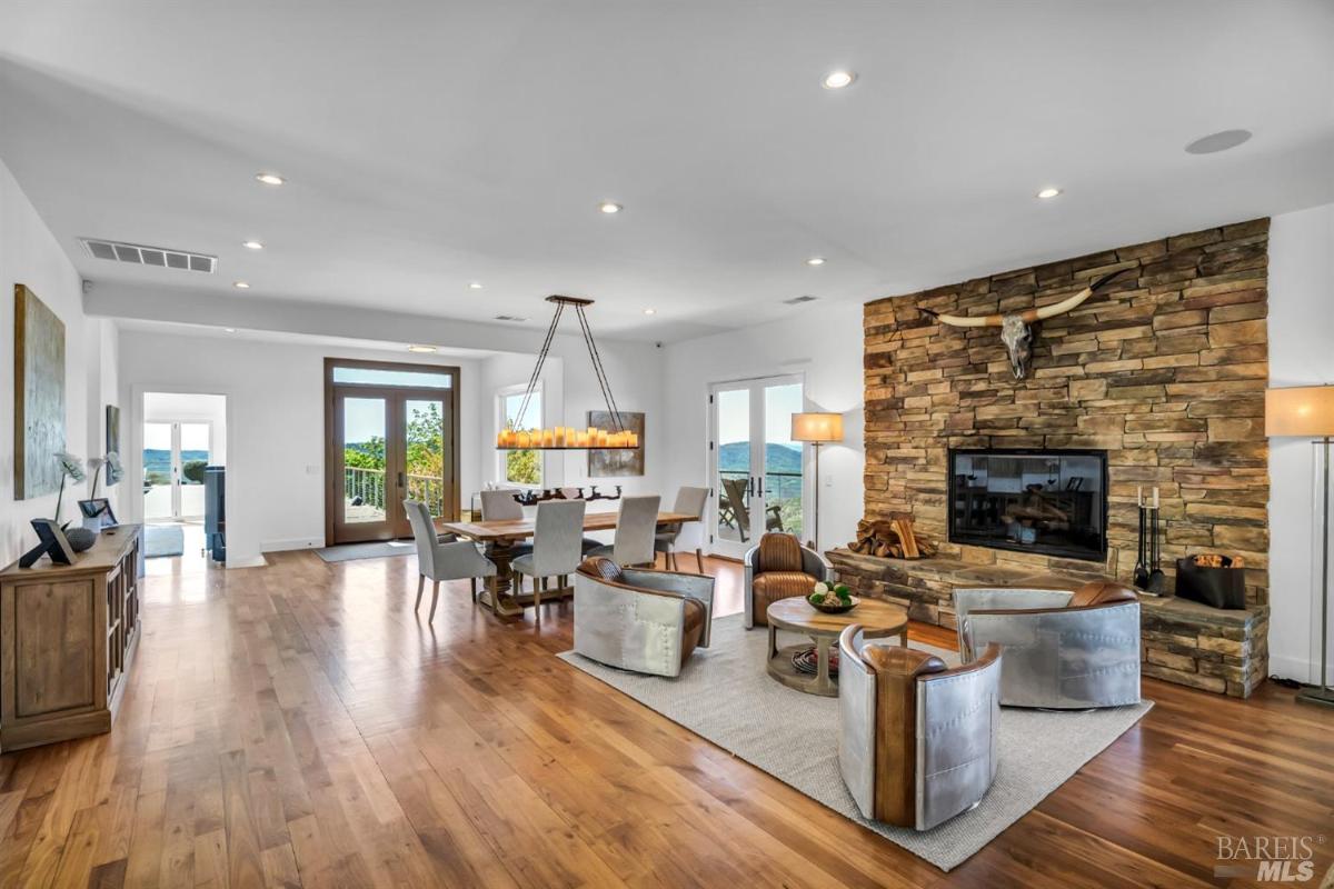 Interior view of a living area with a stone fireplace, dining area, and large windows.