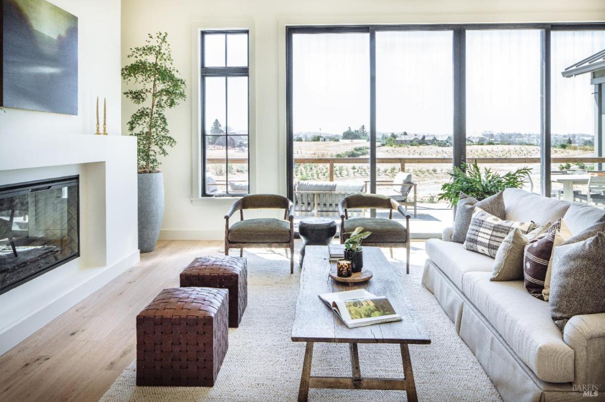 A living room with a fireplace, seating area, and large windows overlooking the landscape.