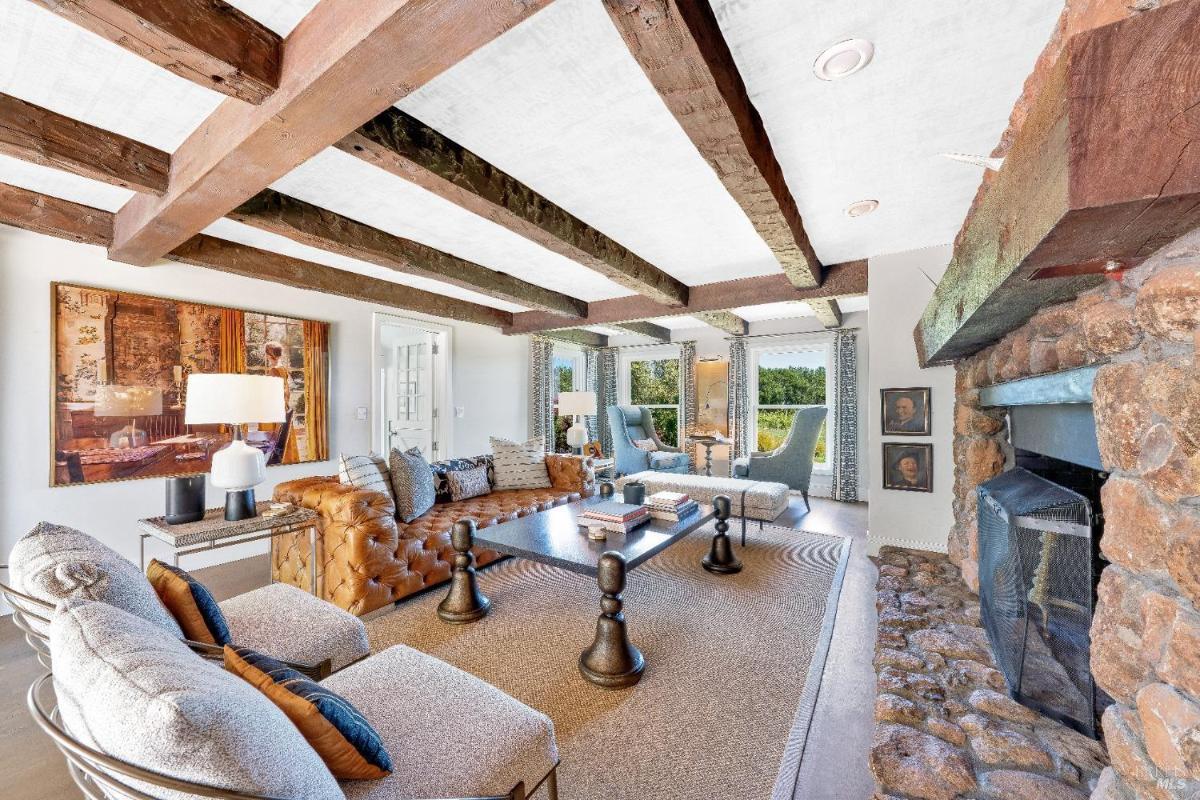 Living room with exposed wooden beams, stone fireplace, and seating area.