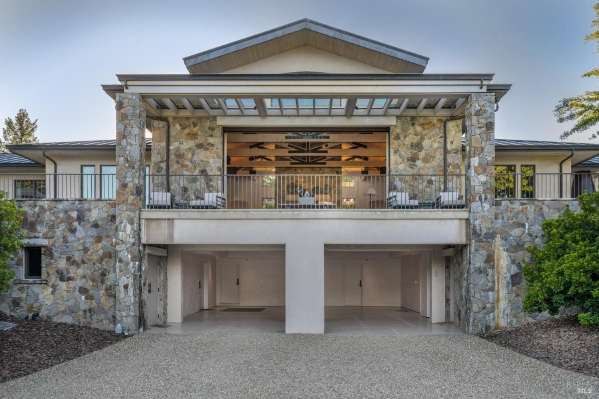 A modern two-story house with a stone facade, featuring a large balcony on the upper level and a spacious garage on the lower level. 