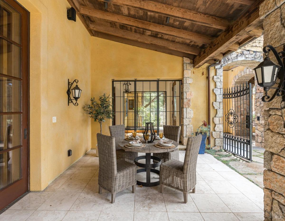 An outdoor covered patio with a dining table, chairs, and decorative lighting.