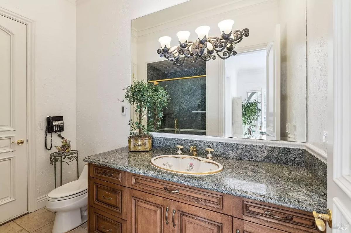 Bathroom with a single vanity, granite countertop, decorative mirror, and access to a shower area.