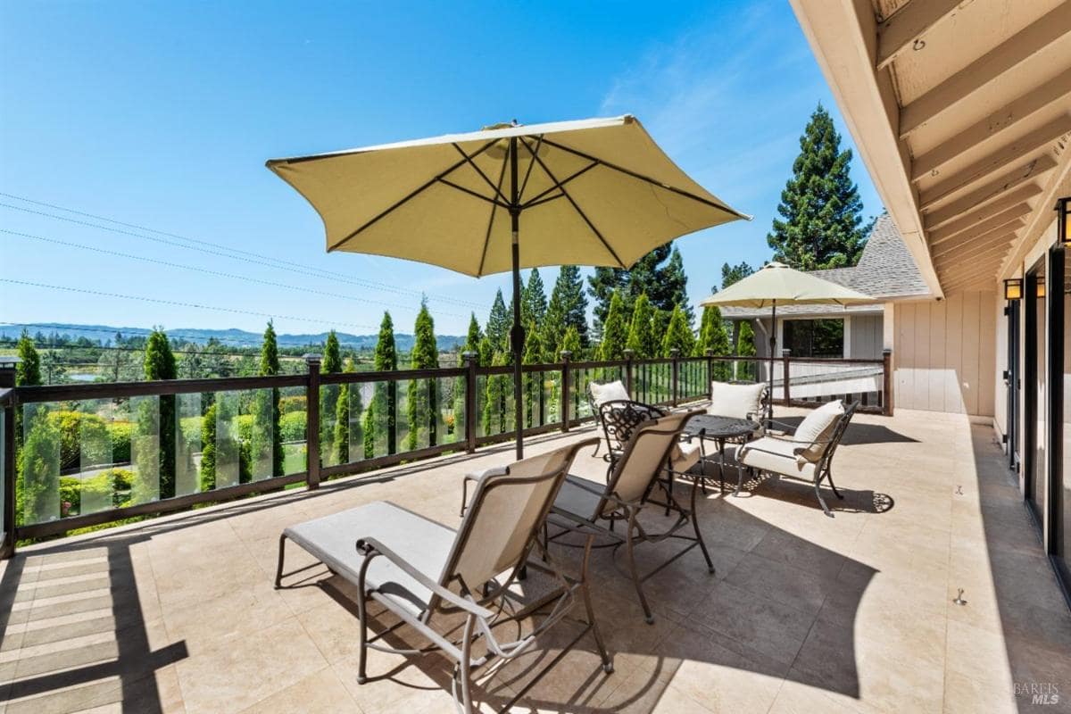 A terrace with lounge chairs and umbrellas overlooking a green landscape and trees.