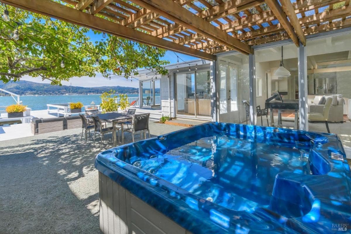 Hot tub under a pergola with view of the house and waterfront deck.