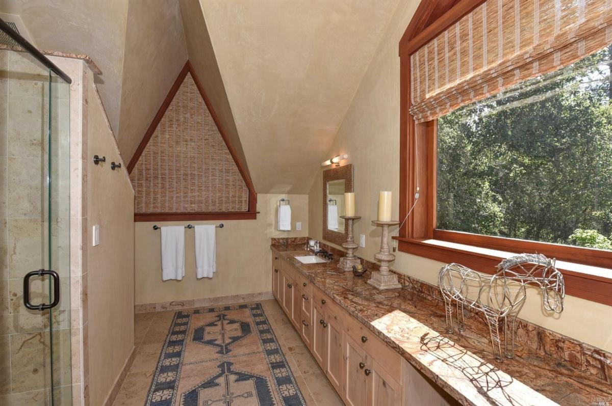 A bathroom with a long double vanity, a large window, and a shower enclosure.