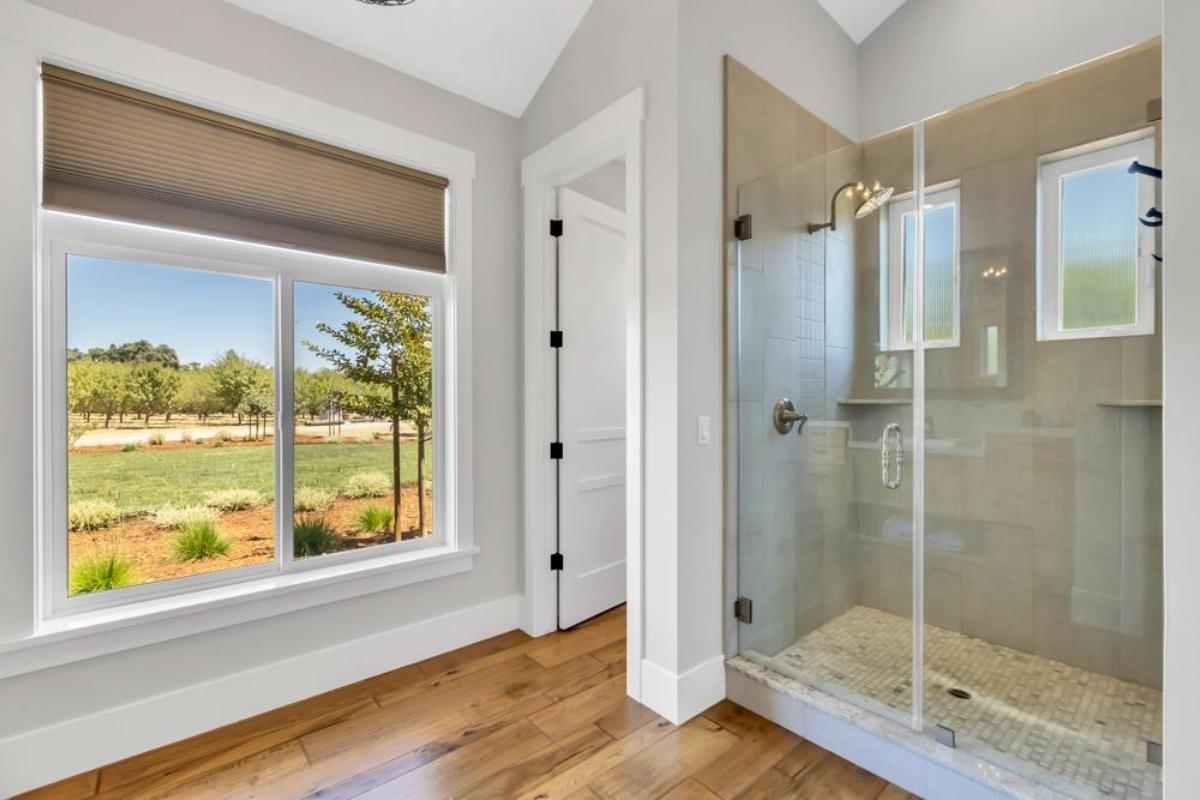 A glass shower is visible next to a window overlooking an outdoor landscape.