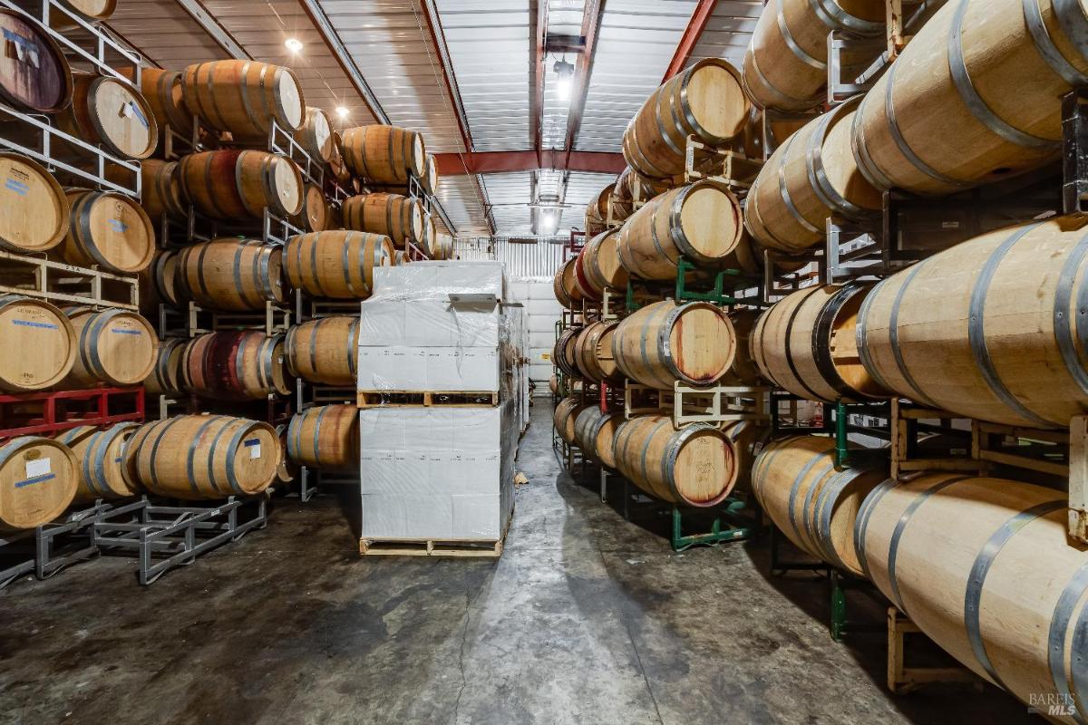 Interior storage area with rows of stacked wooden wine barrels.