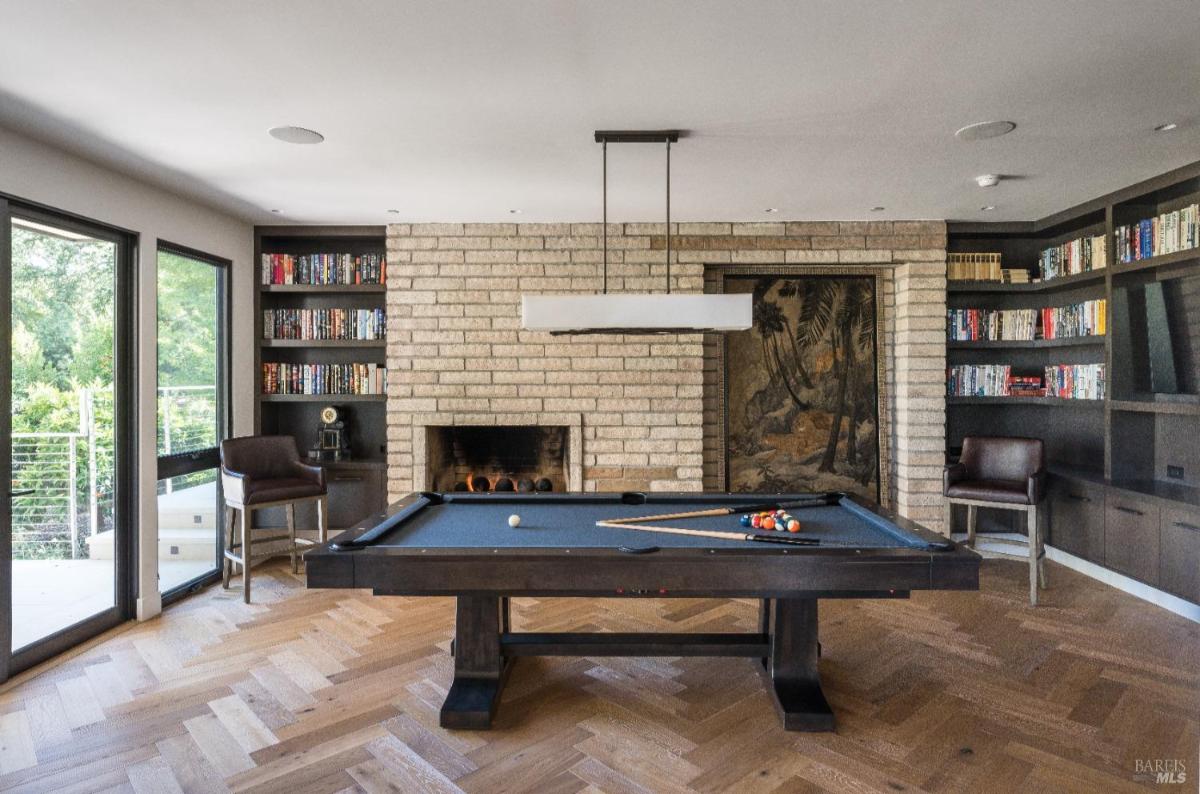 Game room with a billiards table, a brick fireplace, built-in bookshelves, and large windows.