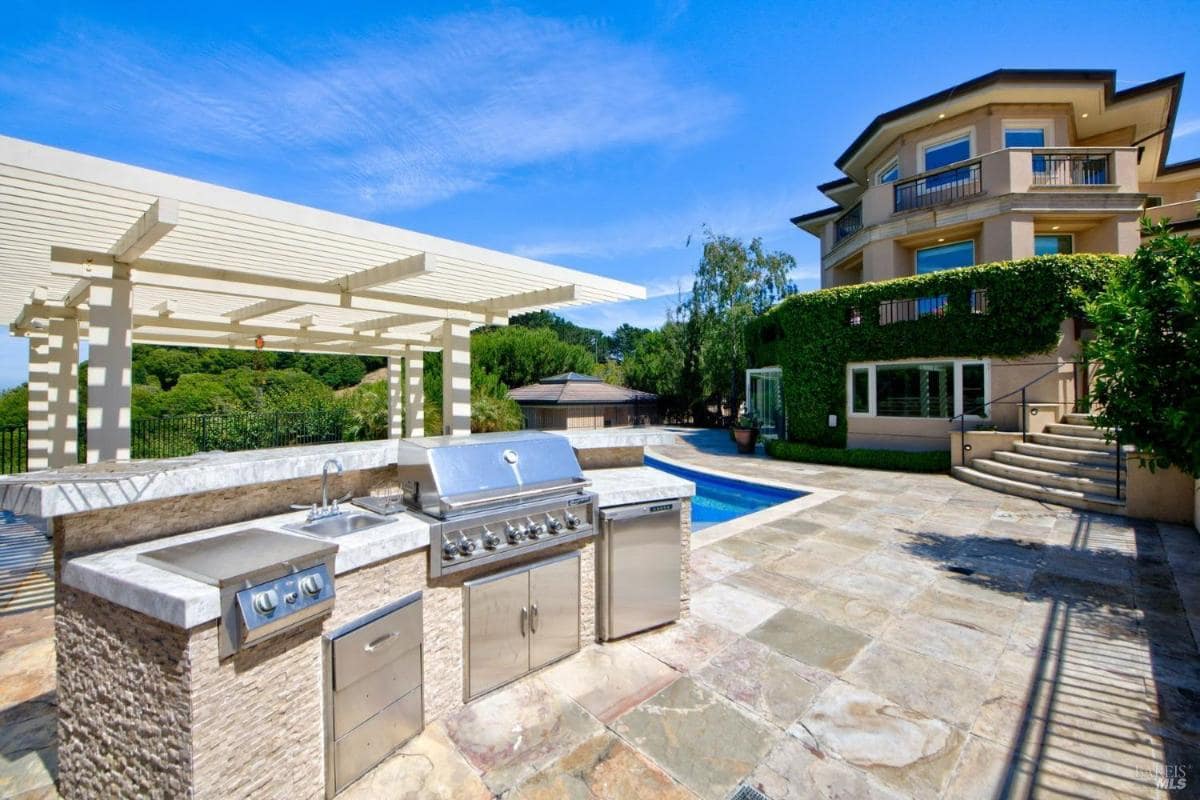 Outdoor kitchen with grill, sink, and counter near a pool.