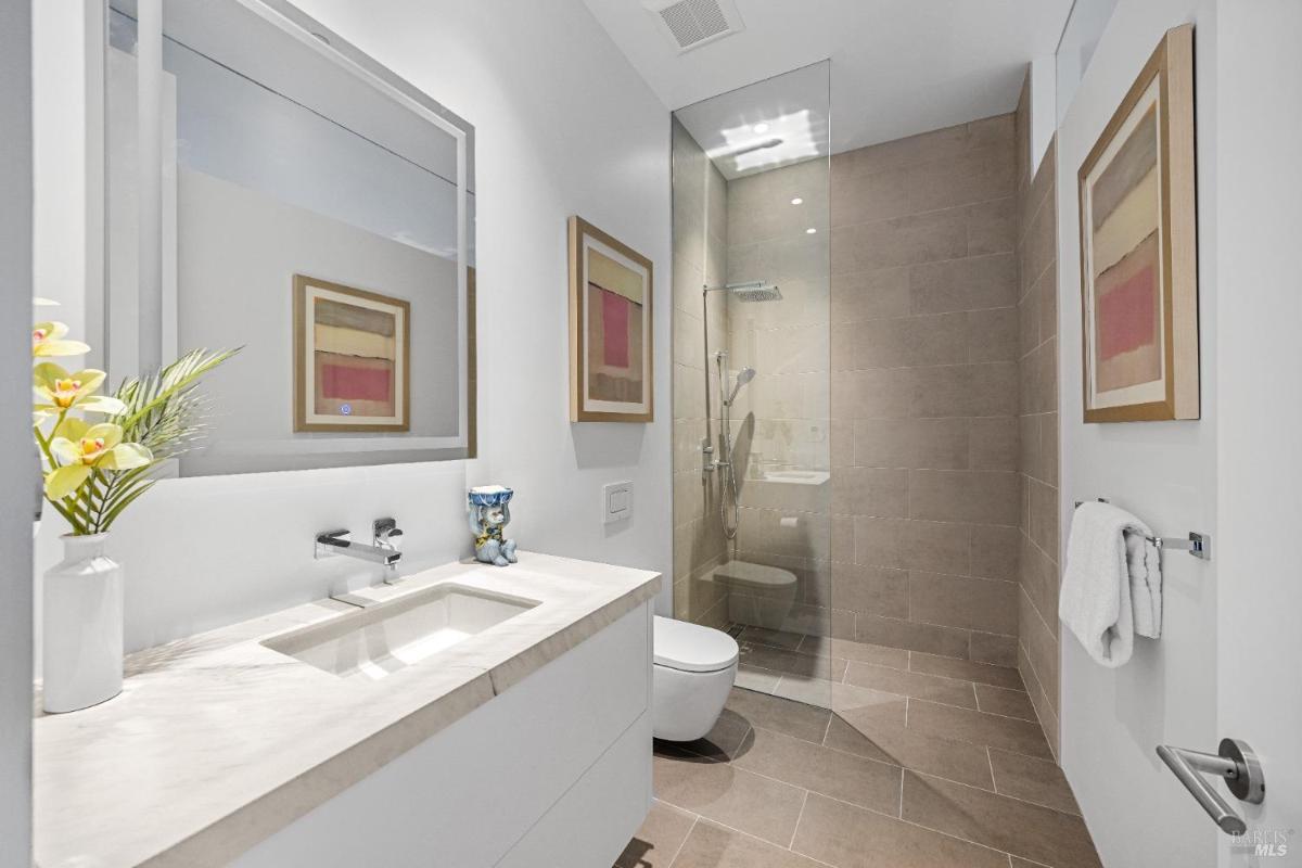 A bathroom with a single-sink vanity, a walk-in shower, and neutral-tone tile walls.