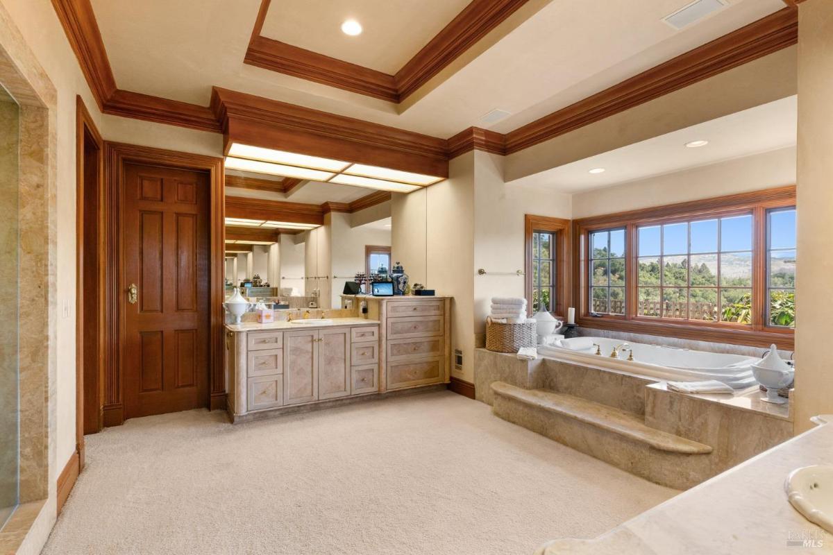 Expansive bathroom with double vanities, soaking tub, and a large window showcasing nature.