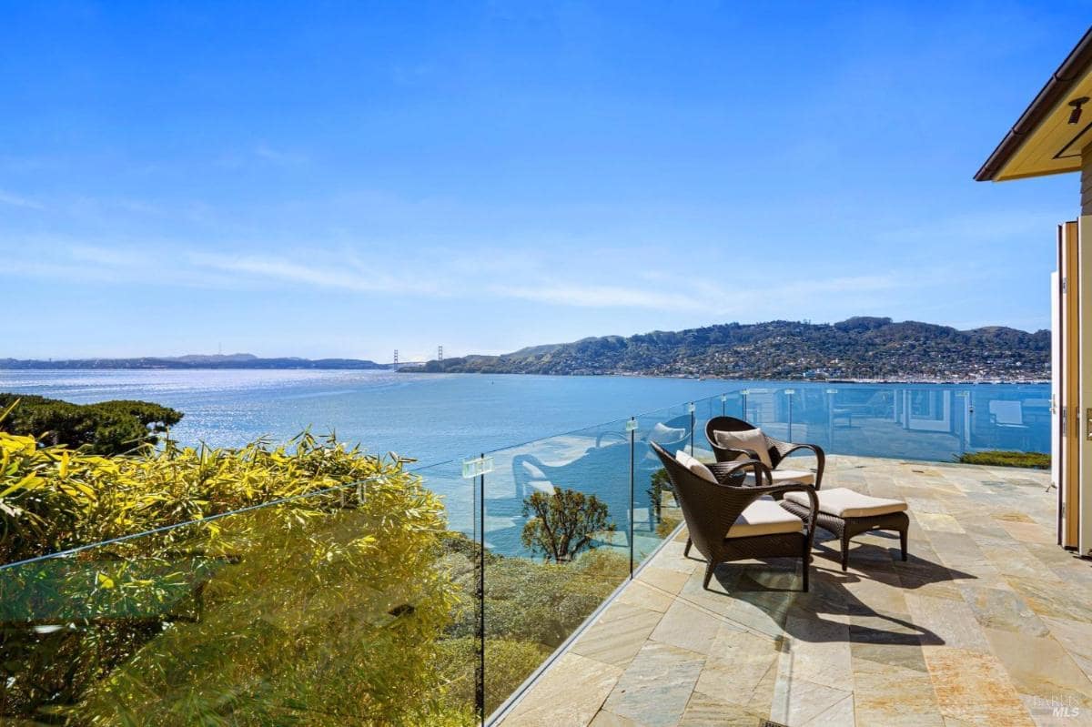 A serene terrace featuring lounge chairs and unobstructed glass railings, overlooking the bay and lush landscape.