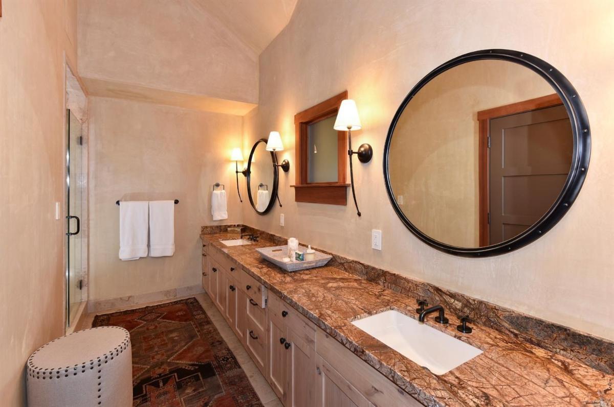 A bathroom with double mirrors, a vanity with a marble countertop, and a walk-in shower.