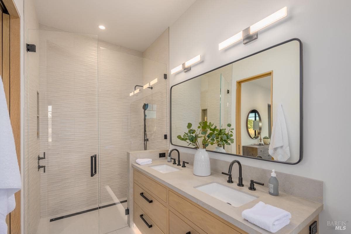 A bathroom with a double vanity, large mirror, and a glass-enclosed walk-in shower.