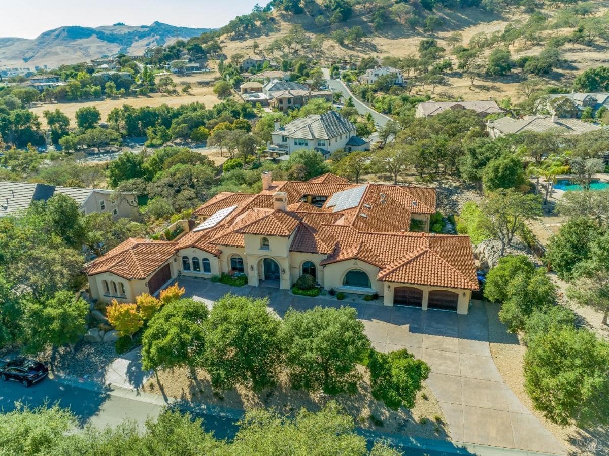 An aerial view of a large house with a tiled roof surrounded by trees and hills.