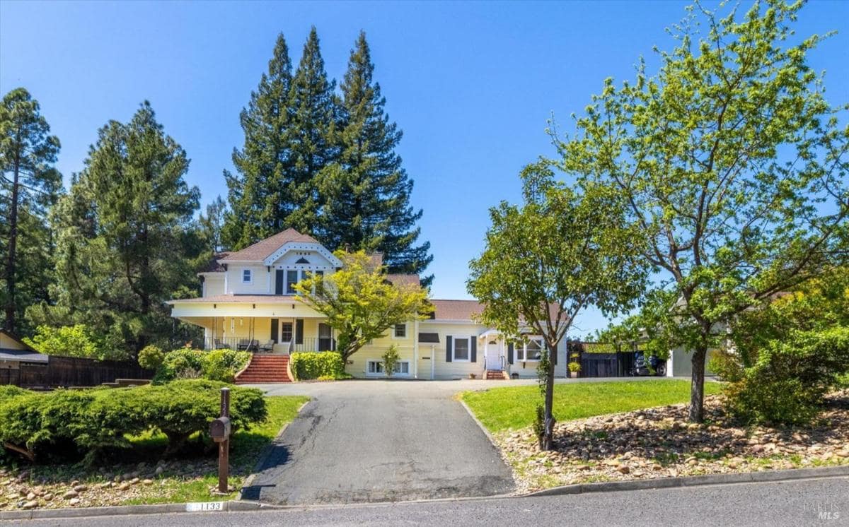 Street view of the house with a landscaped front yard and large trees.