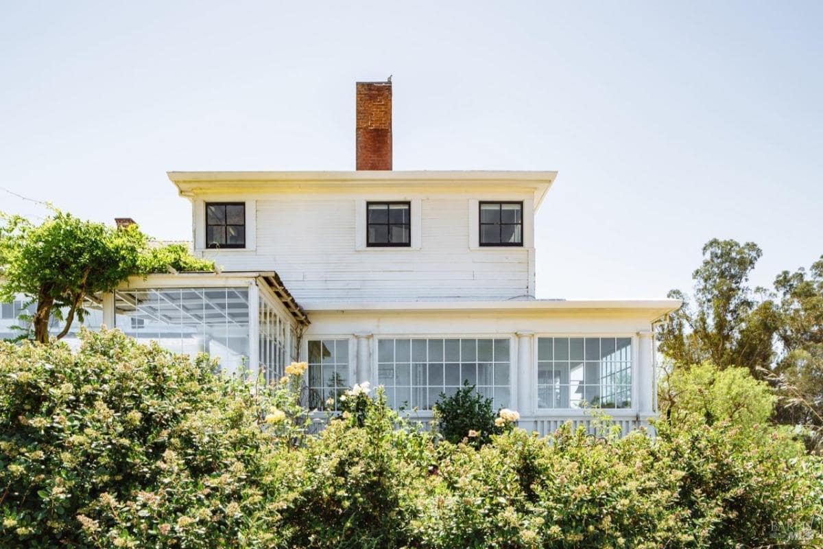 A view of the back of the house with a glass-enclosed sunroom and chimney.