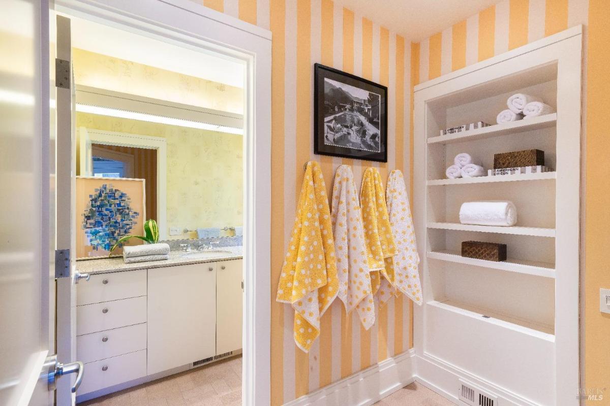 A bathroom with yellow striped wallpaper, a storage shelf, and towels.