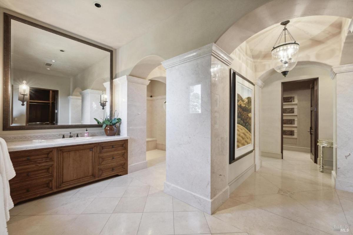 A bathroom featuring marble floors and walls, elegant lighting fixtures, and a wooden vanity with sinks.